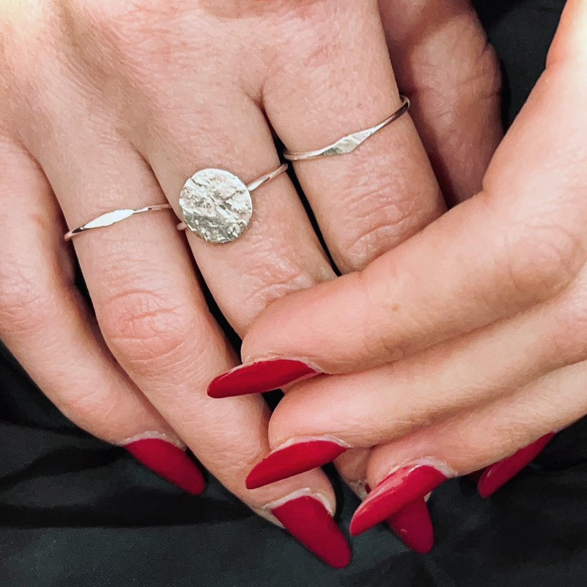 Due sottili anelli di argento ricilato e uno con un piccolo disco sono indossato su una mano con unghie con smalto rosso