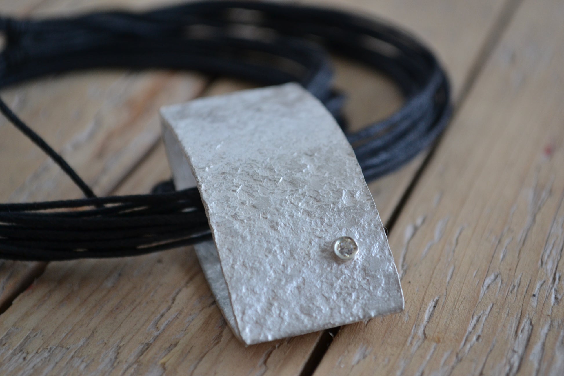Close up of handmade silver pendant with irregular surface and small white zircon