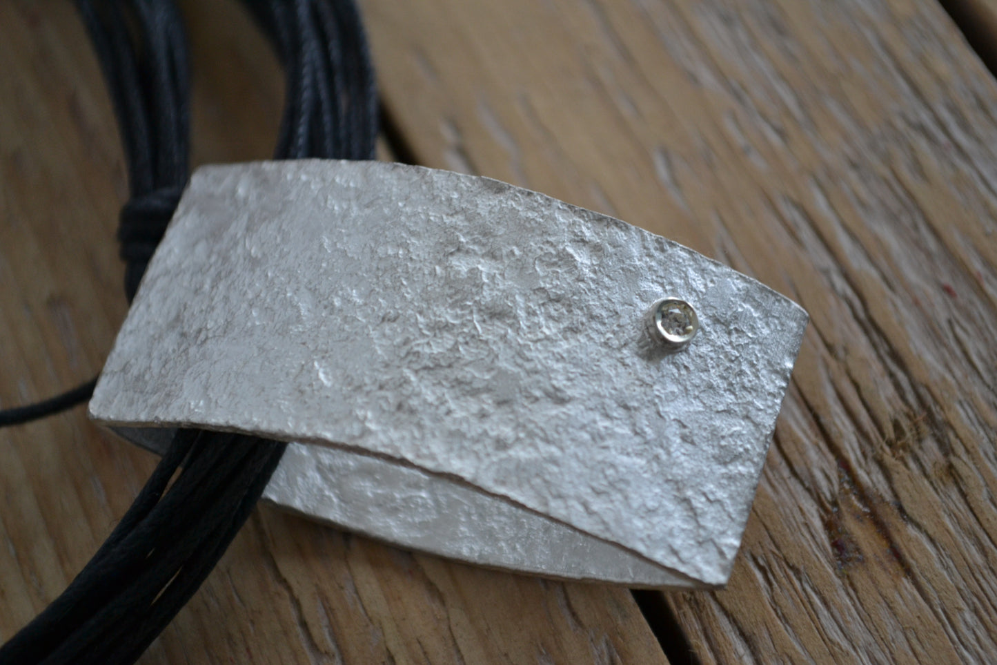 Close up of handmade silver pendant with irregular surface and small white zircon