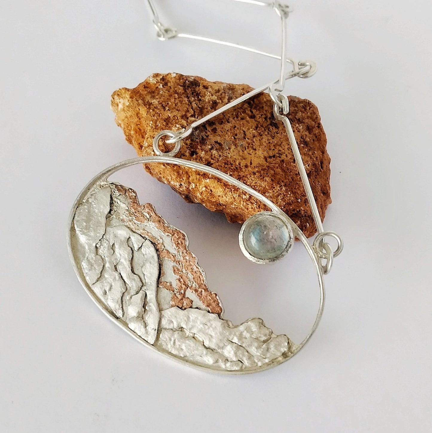 A silver pendant with copper and a moonstone representing a landscape under the moon