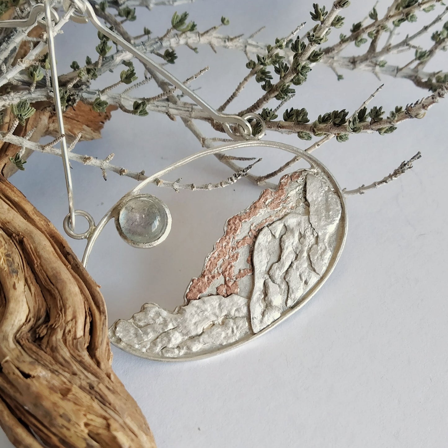 A silver pendant with a labradorite (moonstone) and a copper representing a landscape under the moon