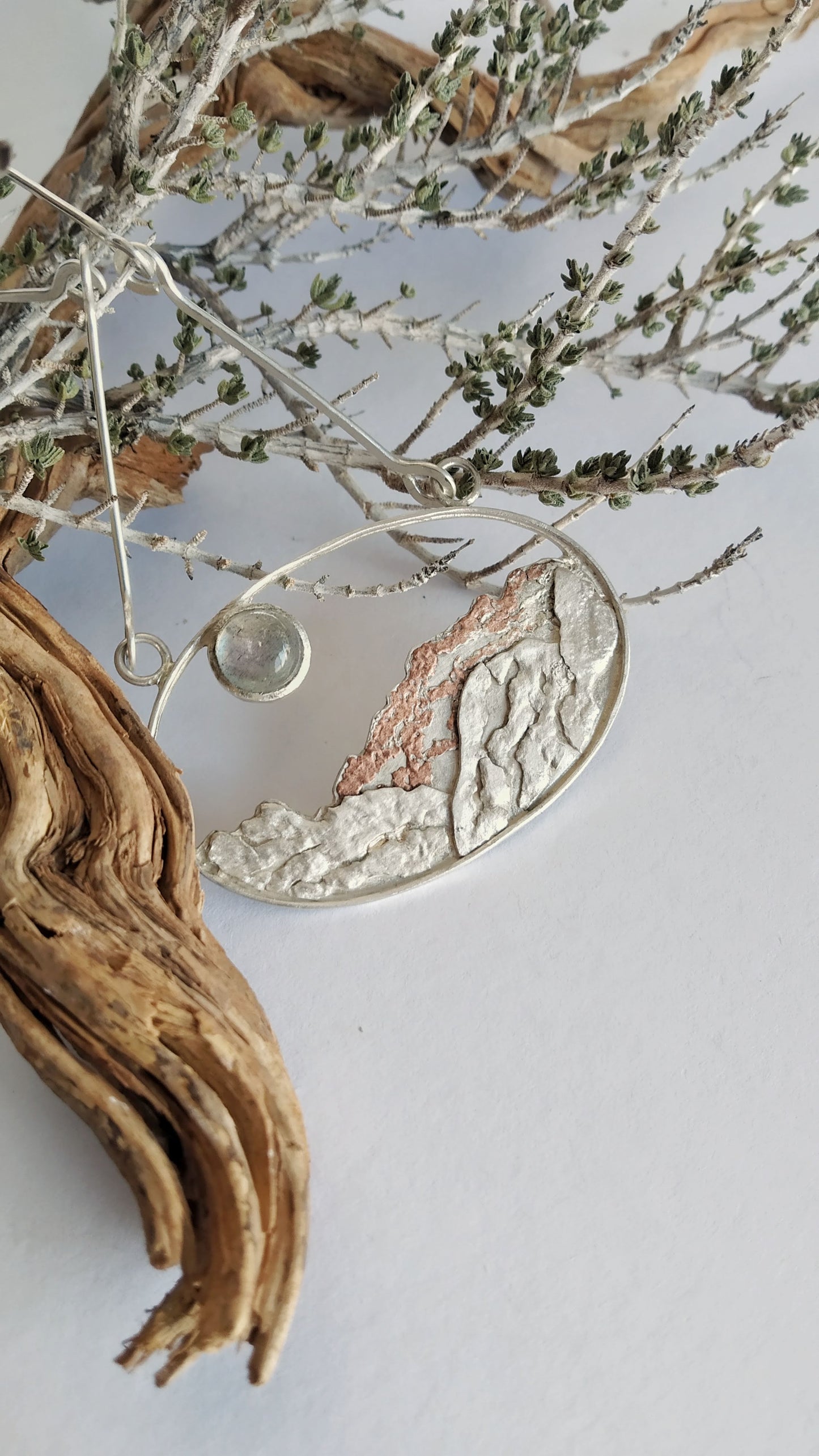A silver pendant with copper and a moonstone representing a landscape under the moon