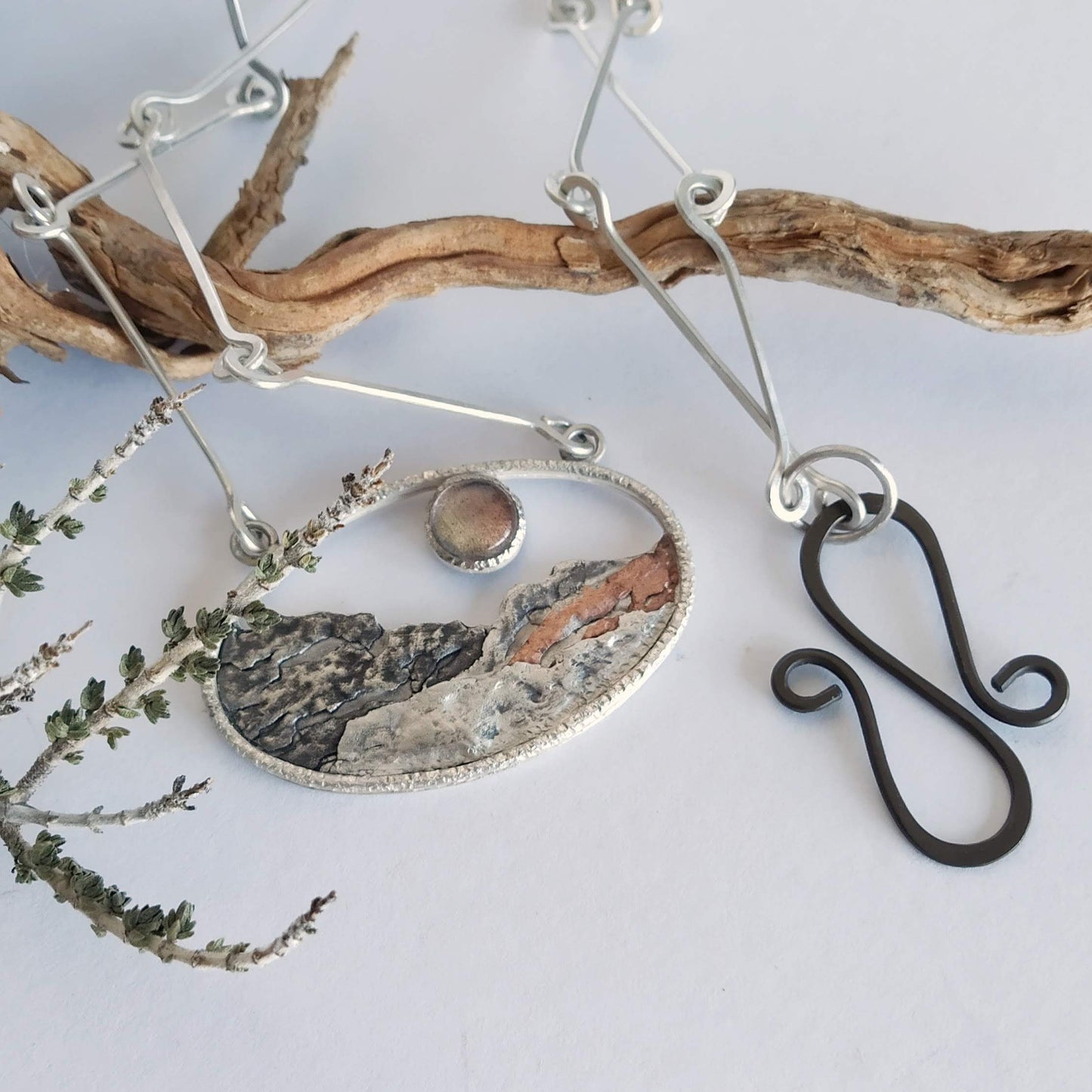 A silver pendant with a labradorite and some copper, representing a landscape at sunset