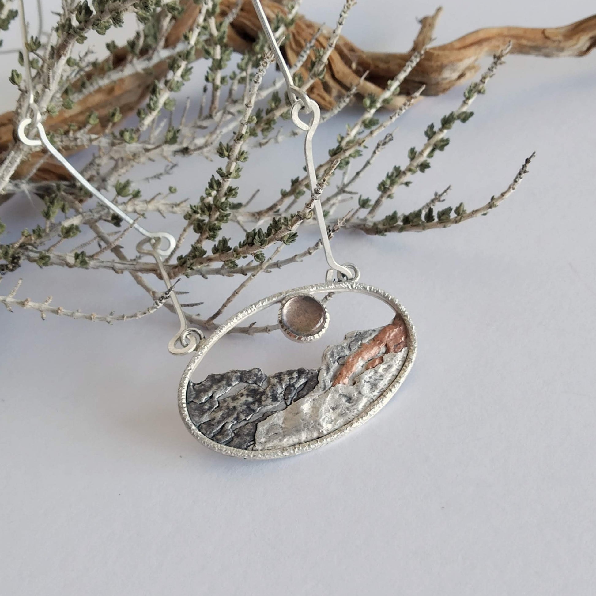 A silver pendant with a labradorite and some copper, representing a landscape at sunset