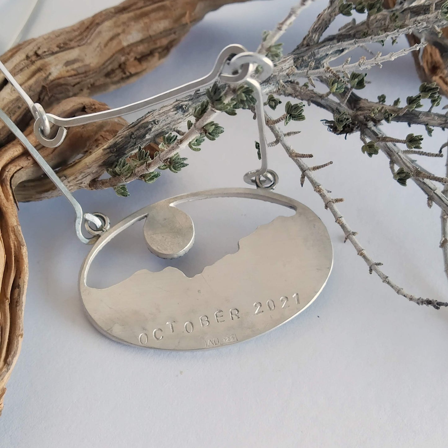 The back of a silver pendant, bearing the date (October 2021). The front of the silver pendant has a labradorite, some oxidized silver layers and some copper, representing a landscape at sunset