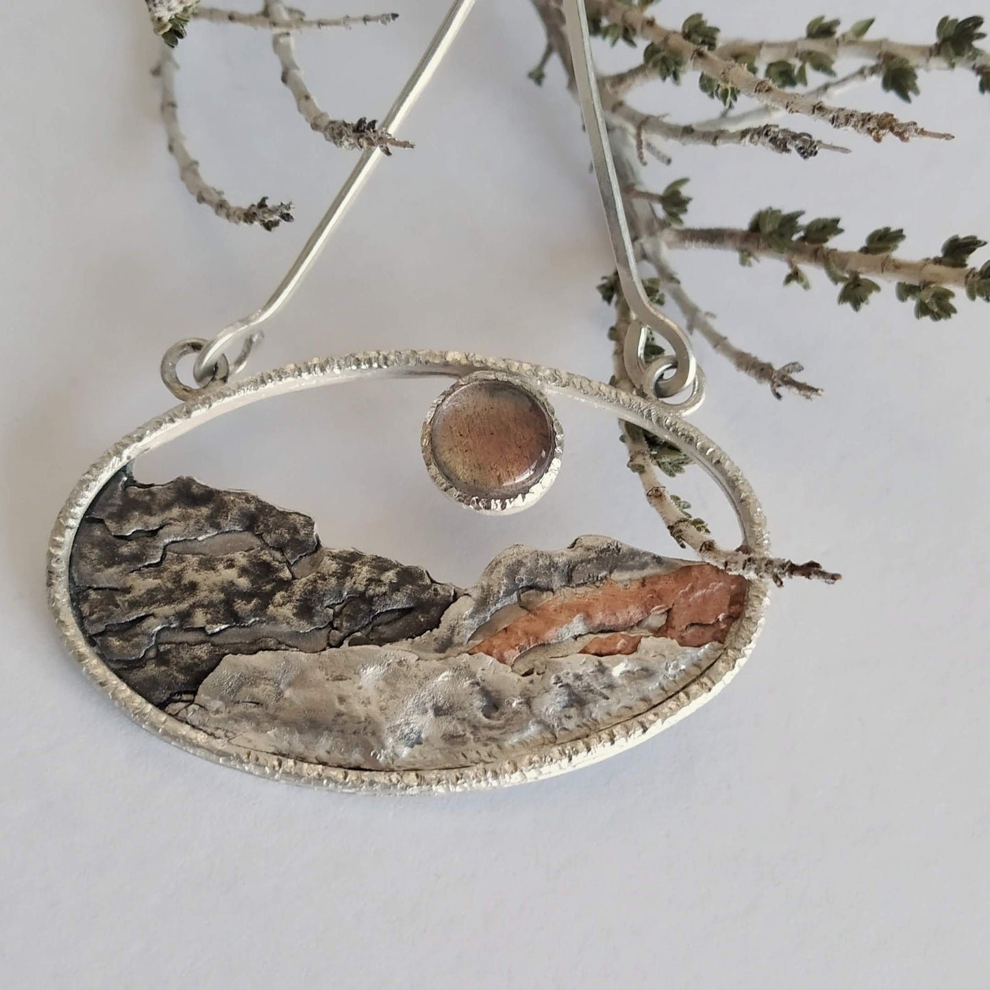 A silver pendant with a labradorite and some copper, representing a landscape at sunset