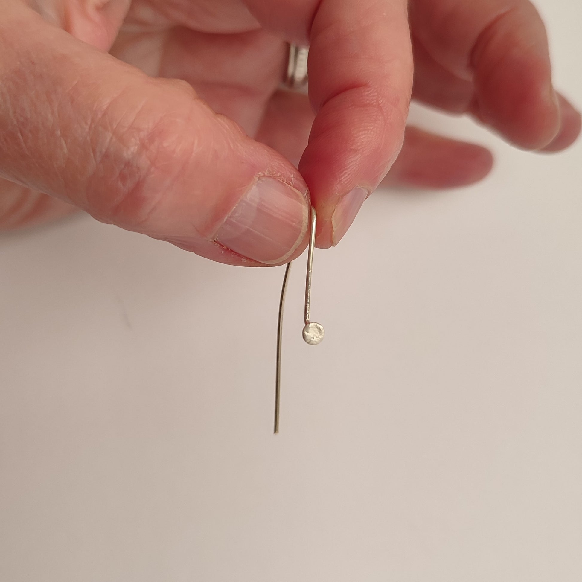 Maker's hand holding a silver earrings hook
