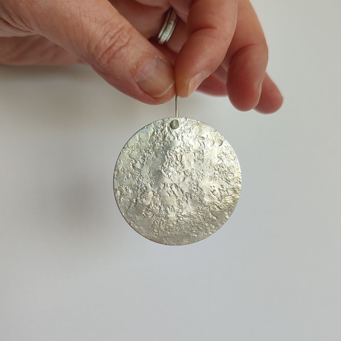 The maker's hand holding one big, round silver earring